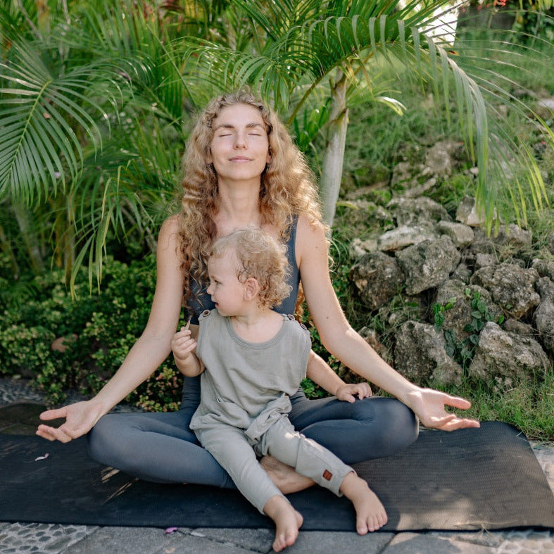 Eine Frau macht Yoga, ein Kind begleitet sie. Bild vermittelt Entspannung und Zufriedenheit